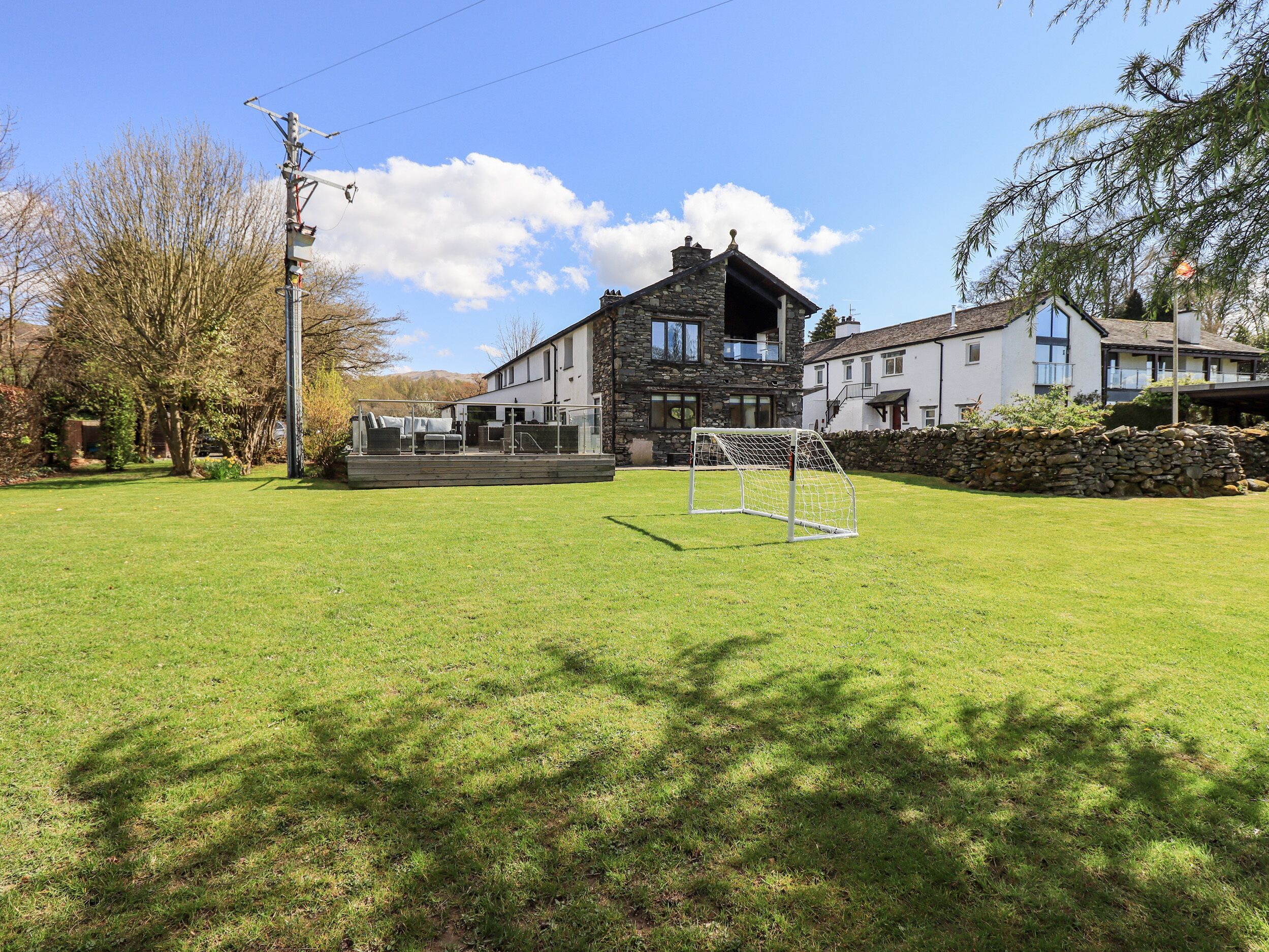 A grassy area with a goalpost, a stone building, and a modern house with a balcony.