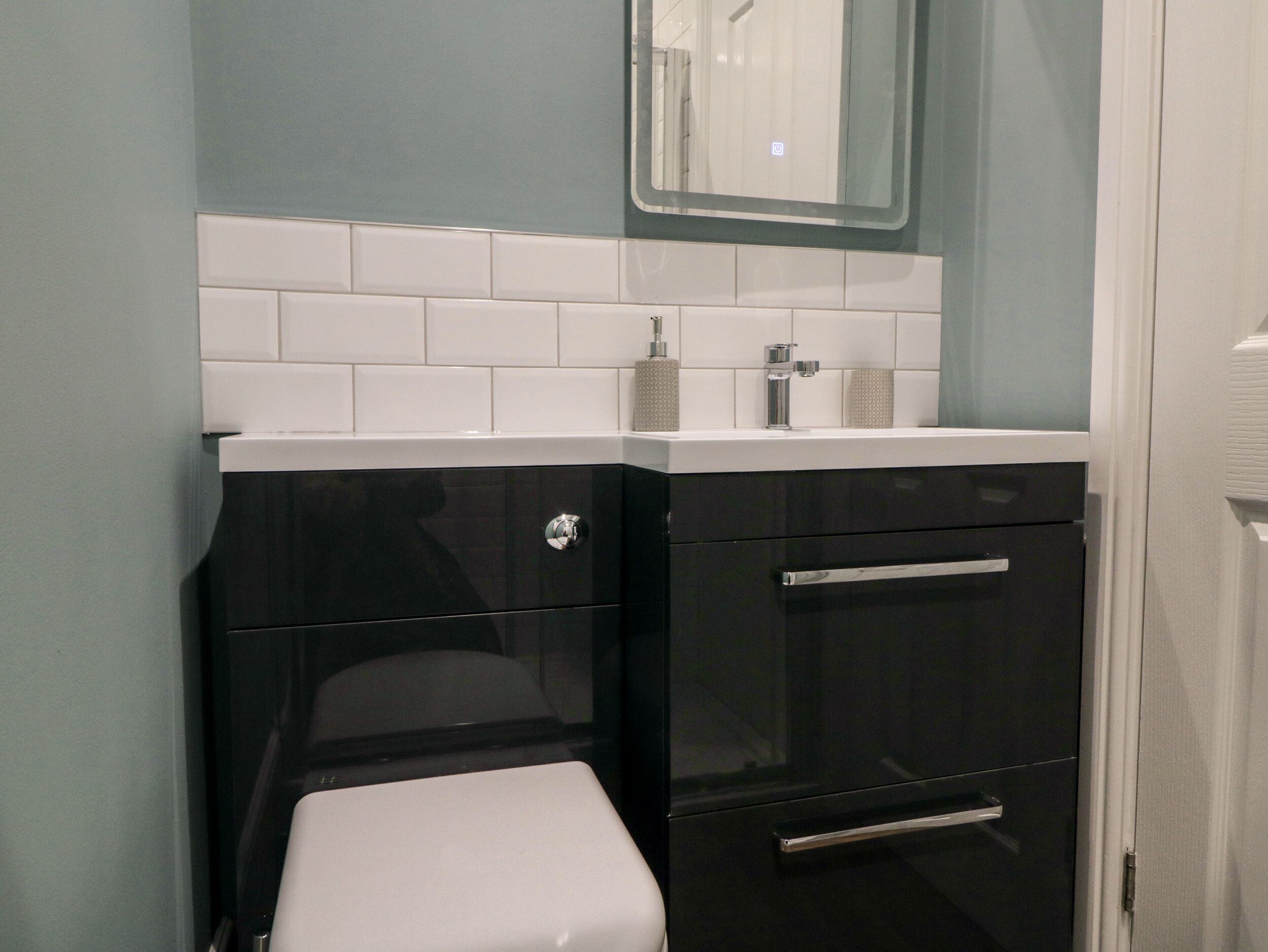 A bathroom with a white toilet, black cabinetry, and a white sink with a mirror above it.