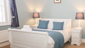 Una camera da letto con un letto bianco, due comodini con lampade, una finestra con tende e un termosifone.