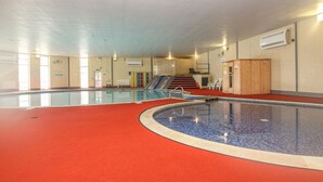 Ein großer, überdachter Pool mit rotem Boden, einer Treppe zu einer erhöhten Ebene und einem Holzkabinett auf der rechten Seite.
