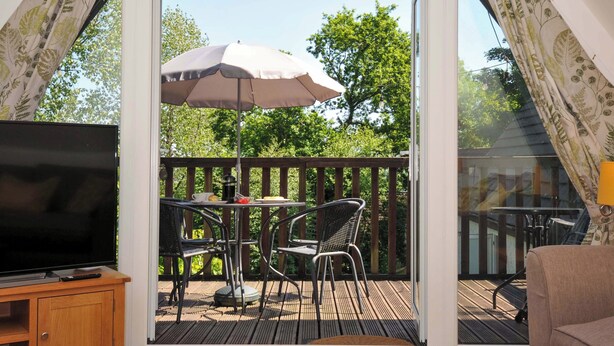 Ein Balkon mit Fernseher, Tisch, Stühlen und Sonnenschirm.