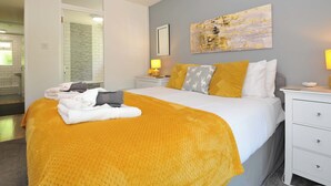 Ein Hotelzimmer mit Bett, Nachttisch, einem Bild an der Wand und einem sichtbaren Badezimmer durch eine offene Tür.