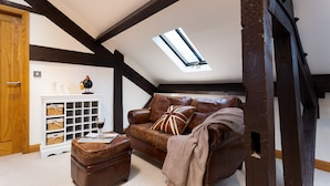 Una habitación estilo loft con un sofá de cuero marrón, un aparador de madera, una copa de vino tinto y un tragaluz.