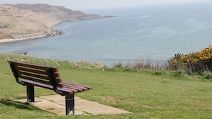 Una panchina con vista sulla costa, sul mare e su dolci colline in lontananza.