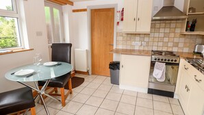 A compact kitchen with a dining table, chairs, a stove, and a trash bin. - Little Stone Howe (Ambleside)