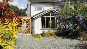 A two-story house with a sloped roof, a wooden deck, and a garden with gravel paths and various plants. - Little Stone Howe (Ambleside)