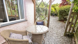 A wicker outdoor seating area with a glass table, surrounded by a gravel path and a wooden fence. - Little Stone Howe (Ambleside)
