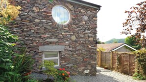 A stone building with a circular window, a small door, and a sign indicating parking. - Little Stone Howe (Ambleside)