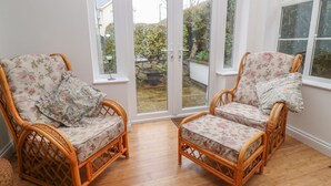 Two wicker chairs with floral upholstery facing a glass door leading to a garden. - Sea Peeps (Paignton)