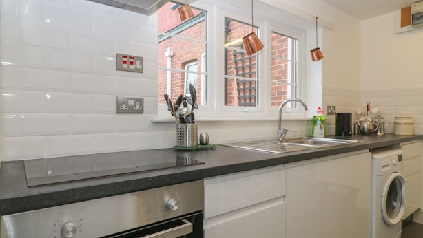 A modern kitchen with a stainless steel oven, a built-in dishwasher, and a window with a view of a brick building. - Sea Peeps (Paignton)