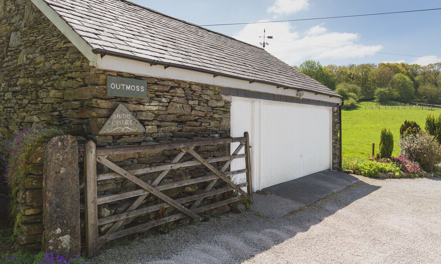 A stone cottage with a white garage door, a wooden gate, and a stone wall.