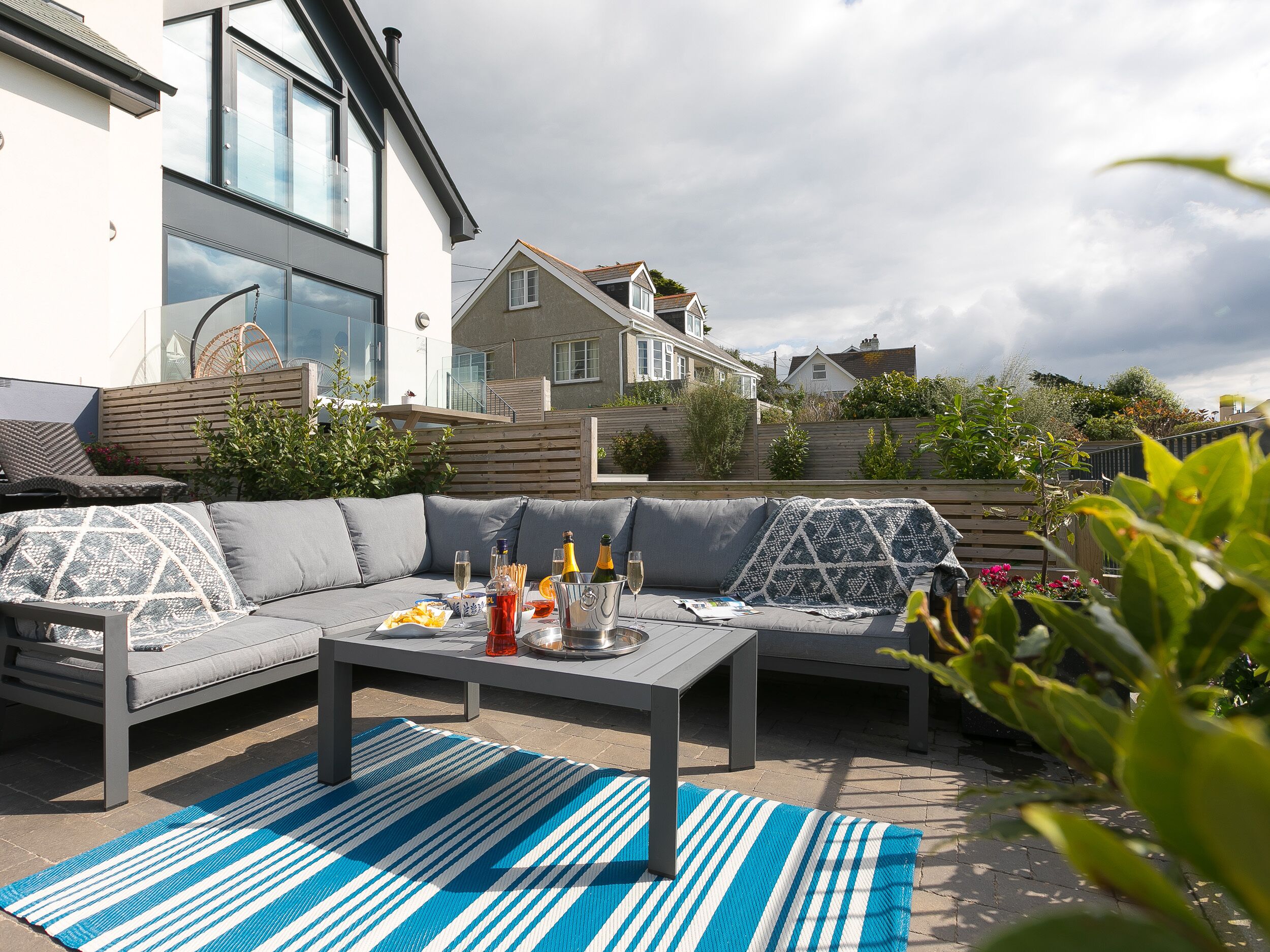 An outdoor seating area with a grey sofa, a coffee table, and a blue-striped rug.