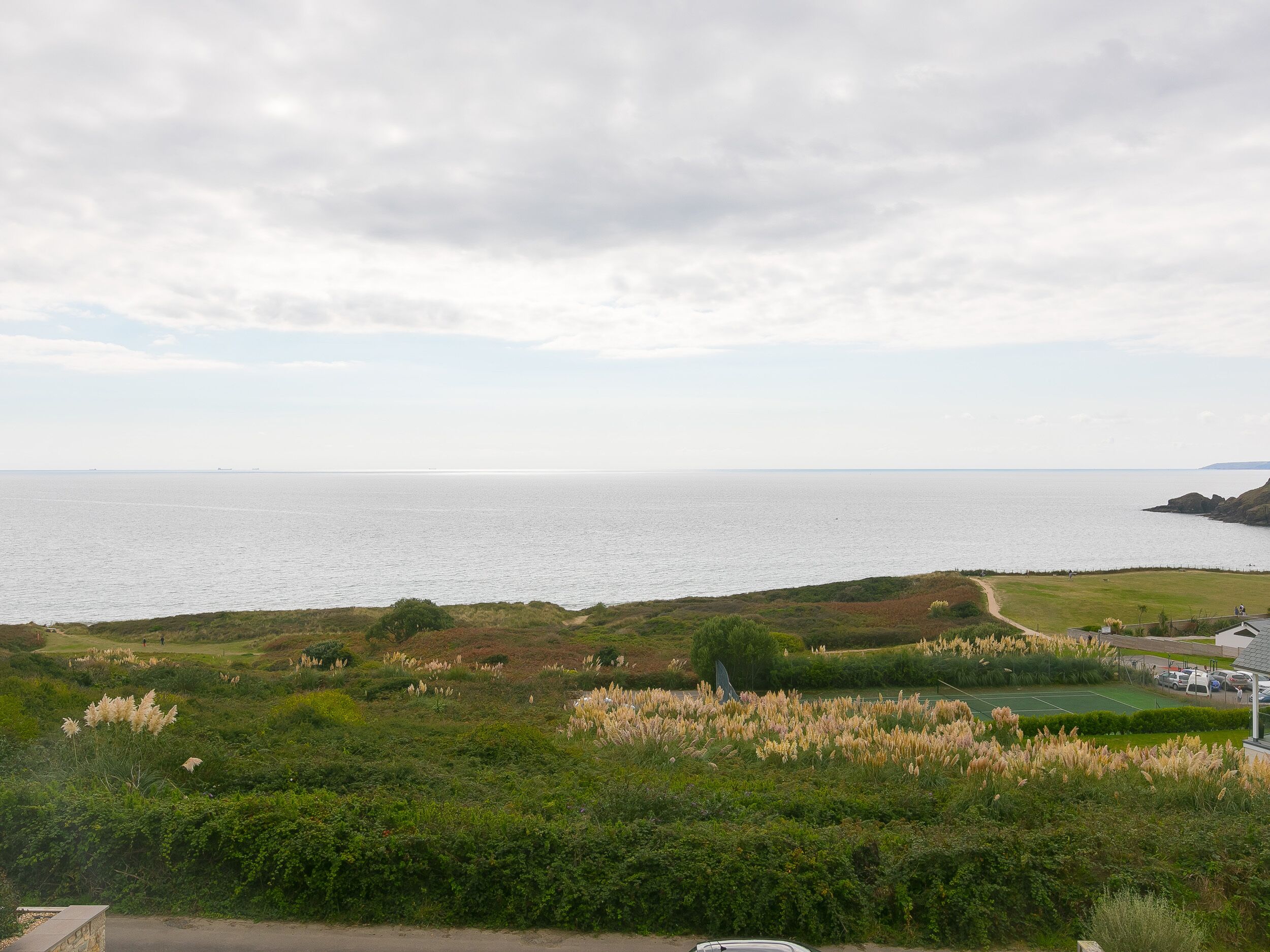 Un paisaje costero con vista al mar, zonas de césped y un estacionamiento.