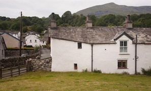 A white building with a gabled roof, a small window, and a door. - Sunbeam Cottage (Coniston)