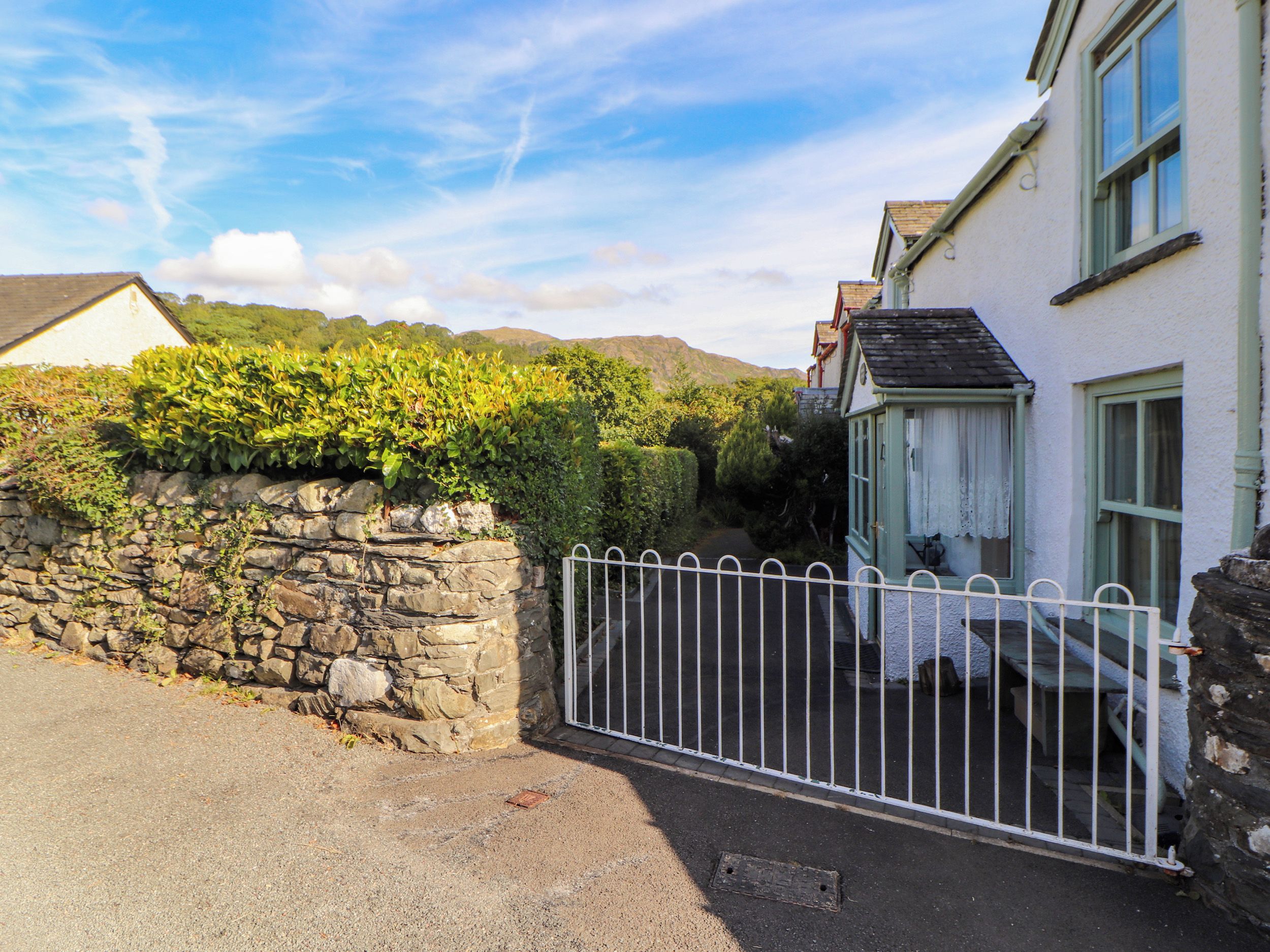 A stone wall with a metal gate, a white building with a green window, and a clear sky.