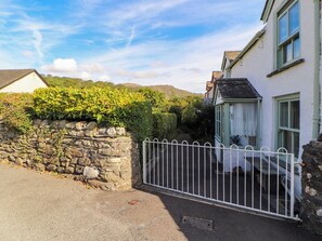 A stone wall with a metal gate, a white building with a green window, and a clear sky.