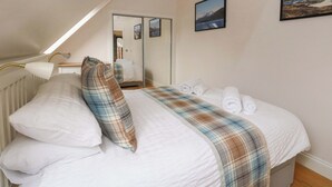 A bedroom with a bed, a bedside lamp, a mirror, and a painting on the wall. - The Apartment (Fort William)