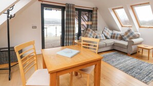 A cozy living room with a sofa, a dining table, and a view of a balcony. - The Apartment (Fort William)