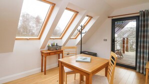 A room with a sloped ceiling, skylights, a wooden table, chairs, a coat rack, and a door leading outside. - The Apartment (Fort William)