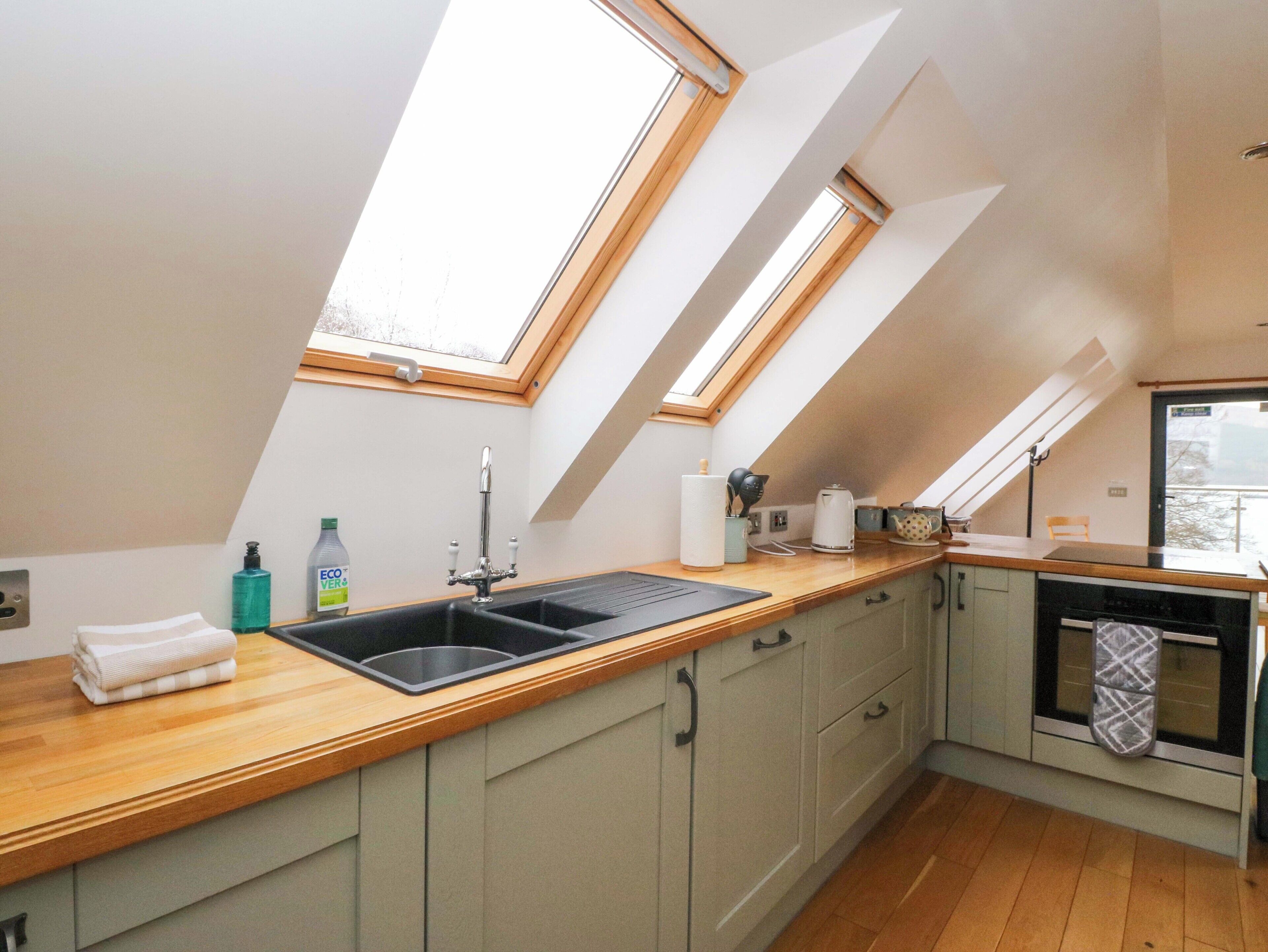 A kitchen with a skylight, a sink, a stove, and a window.