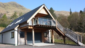 A wooden cabin with a balcony and a staircase leading to a garage. - The Apartment (Fort William)