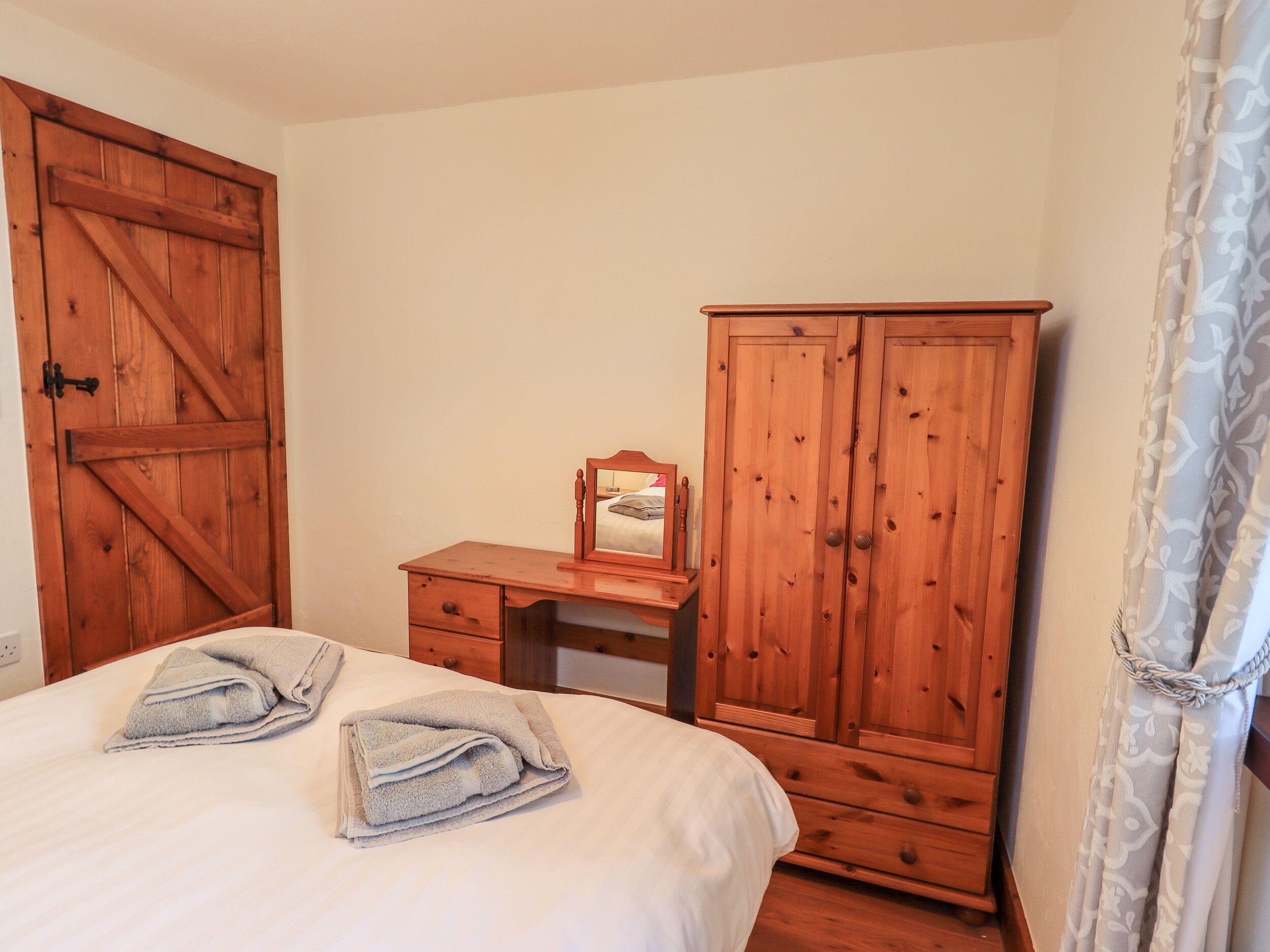 Une chambre à coucher avec un lit, un bureau en bois, un miroir et une armoire.