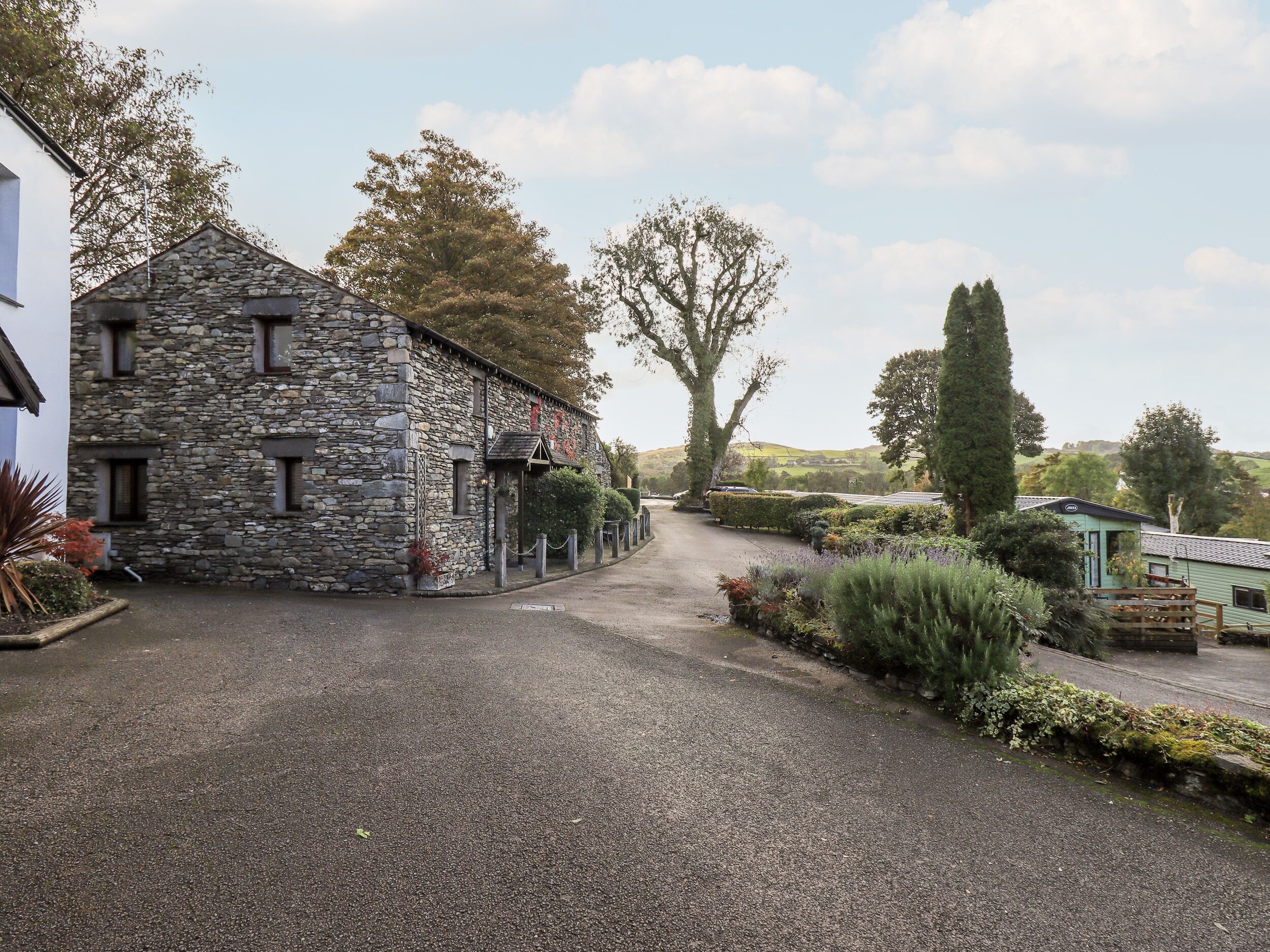A stone building with a gravel driveway, surrounded by greenery and trees.