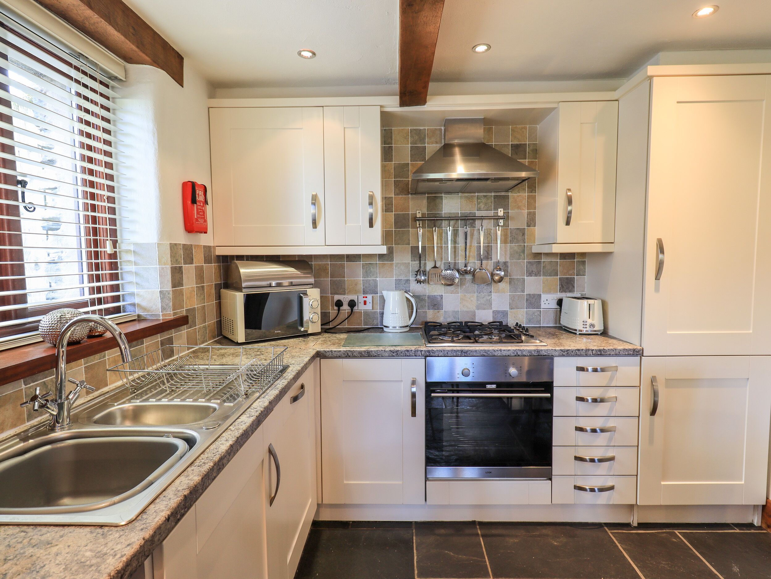 A modern kitchen with white cabinets, stainless steel appliances, a gas stove, a built-in oven, and a window with blinds.