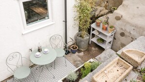 Une petite terrasse extérieure avec une table et des chaises, une fenêtre et des plantes en pot.
