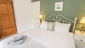 Un lit bien fait, avec du linge de lit blanc et deux oreillers, une armoire en bois, une table de chevet avec une lampe et un tableau encadré au mur.