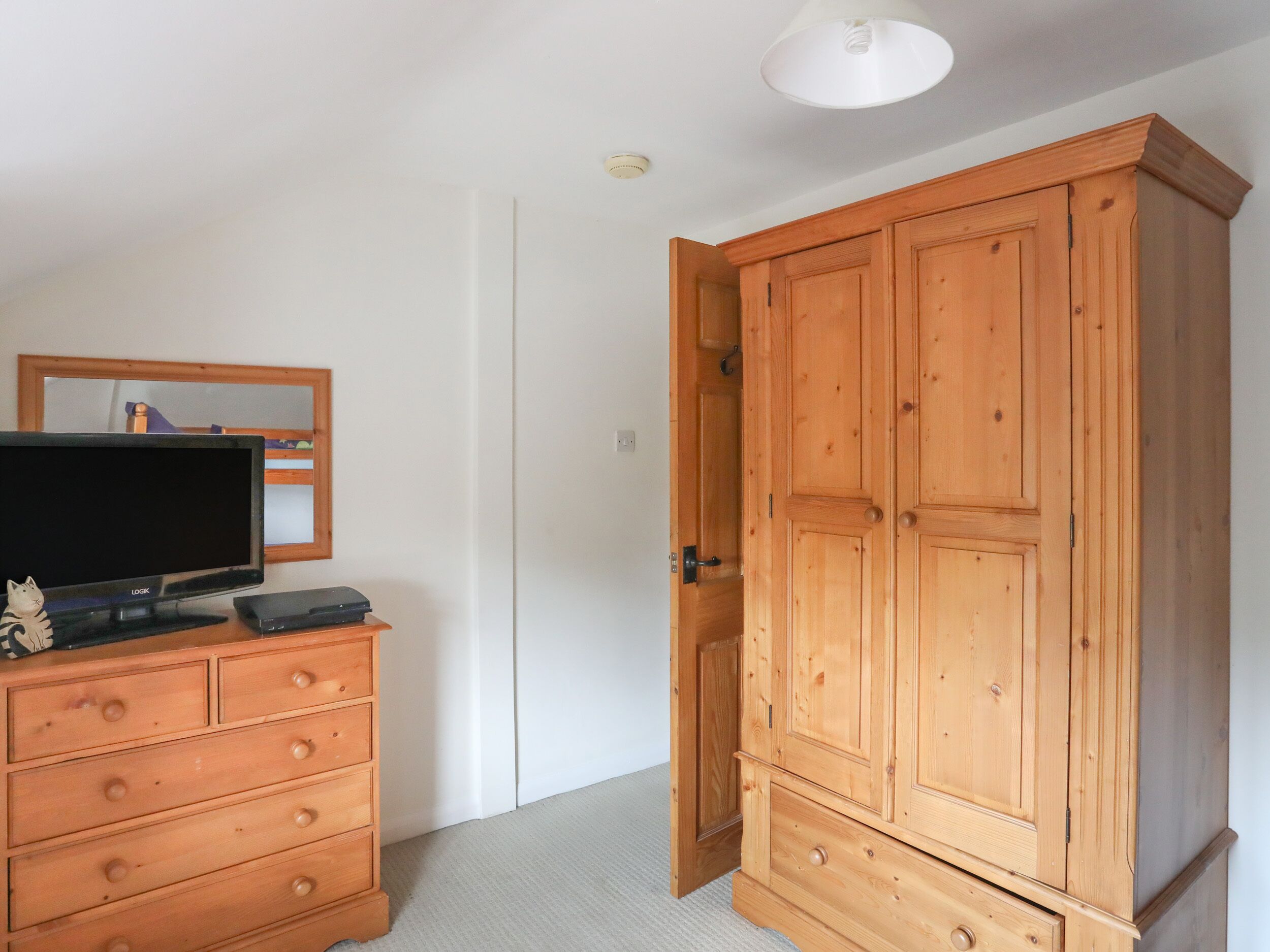 Une pièce avec une armoire en bois, un téléviseur posé sur une commode et un miroir au mur.