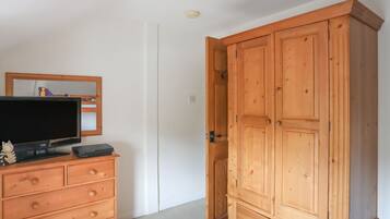 Une pièce avec une armoire en bois, un téléviseur posé sur une commode et un miroir au mur.