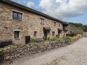 A stone building with multiple windows and doors, a gravel driveway, and a stone wall with plants.