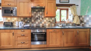 A kitchen with wooden cabinets, a microwave, a toaster, a sink, and a Bosch oven. - Tullythwaite Garth (Kendal)