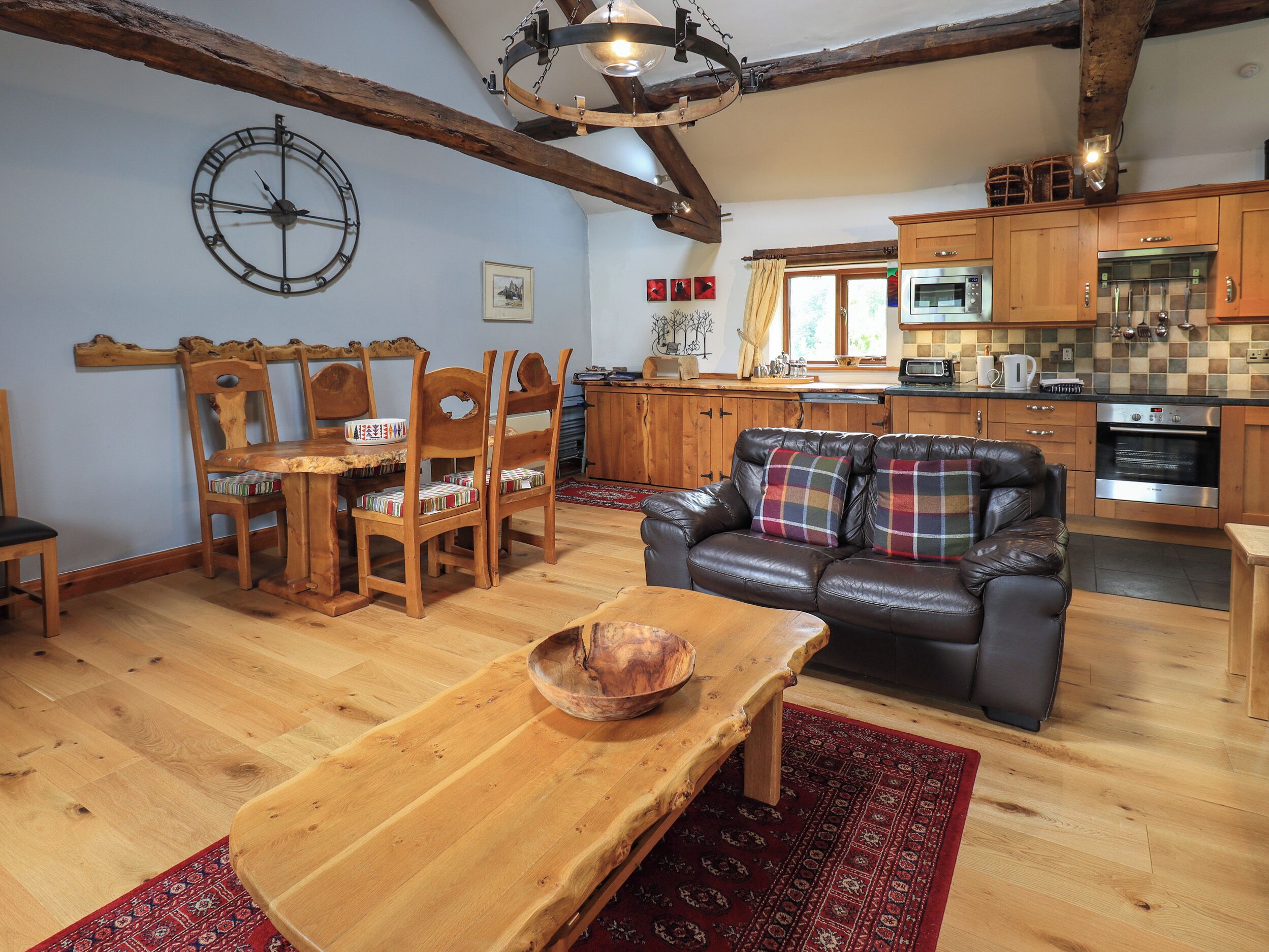 A cozy living room with a wooden dining table, leather sofa, and a rustic ceiling beam.