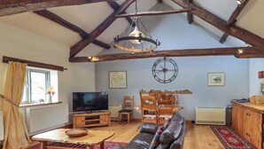 A cozy living room with a leather sofa, wooden coffee table, and a TV. There's a dining area with a wooden table and chairs, and a large clock on the wall. - Tullythwaite Garth (Kendal)