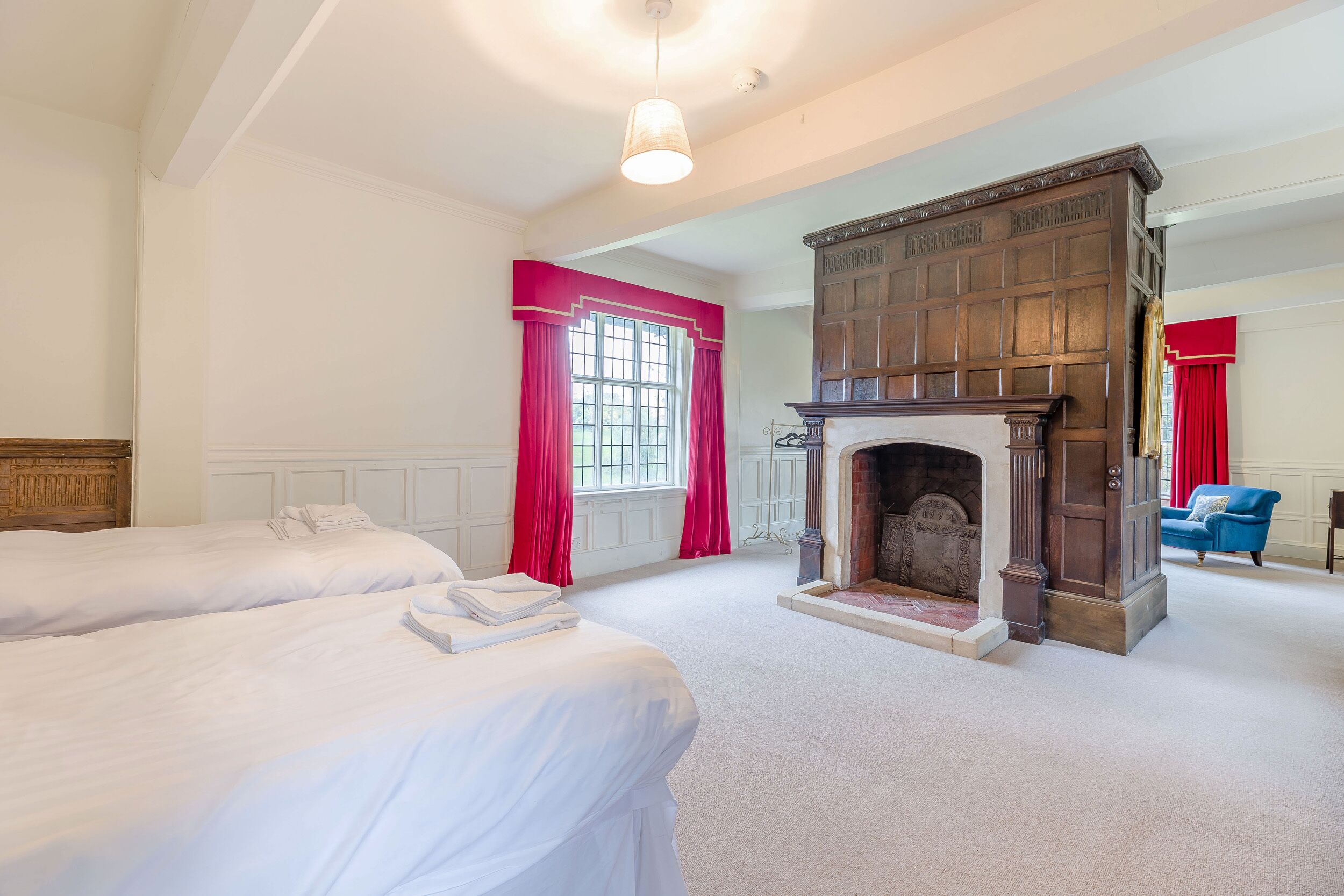 A hotel room with two beds, a fireplace, and a window with red curtains.