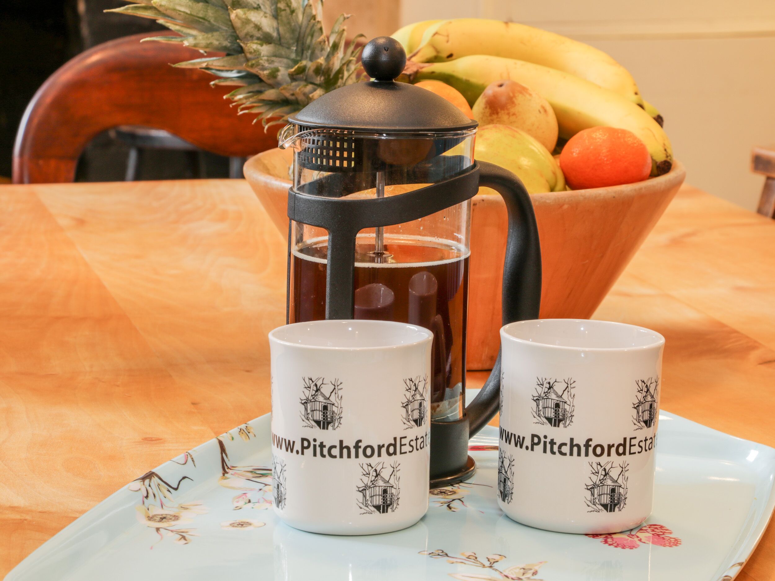 Eine Kaffeekanne, zwei Tassen und eine Obstschale auf einem Tisch.