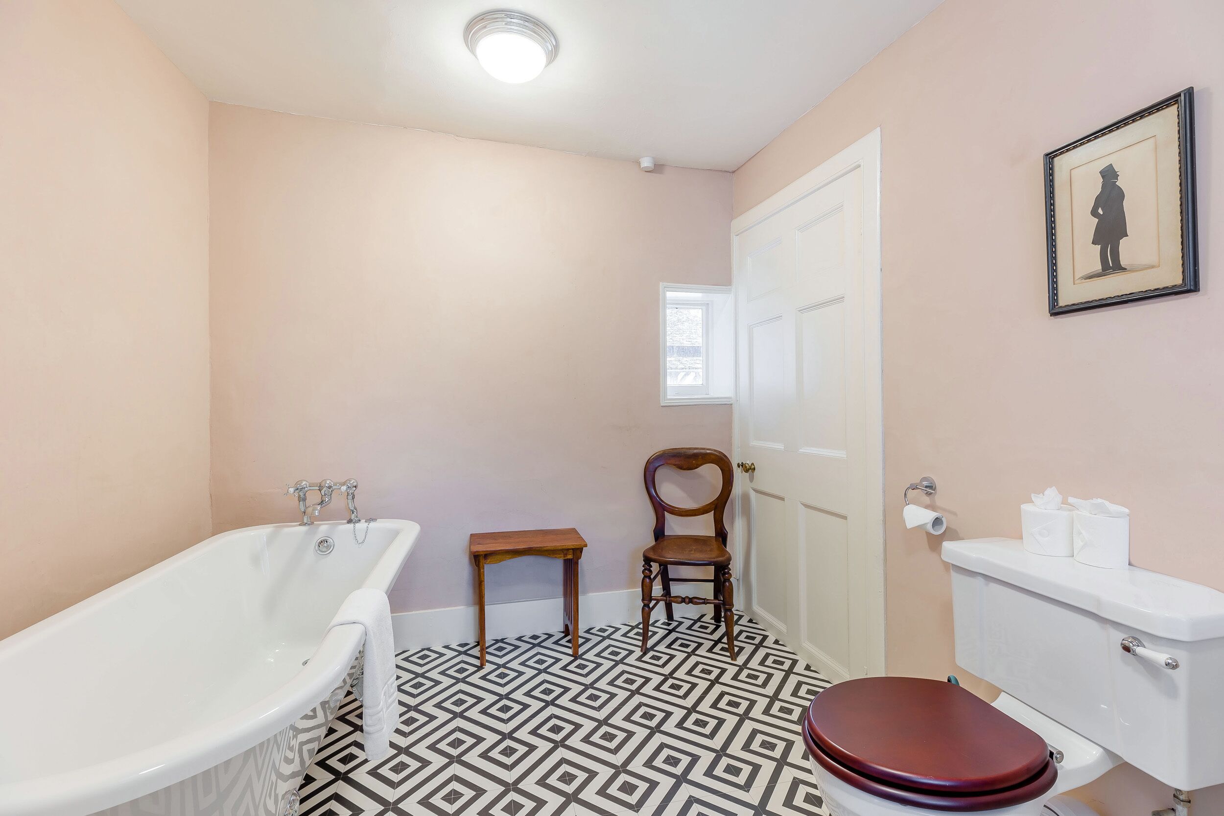 A bathroom with a freestanding bathtub, a wooden chair, a toilet, and a framed picture on the wall.