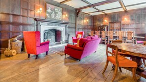 Una habitación amplia con una gran mesa de comedor de madera, dos sofás rojos y una chimenea con un mural en la parte superior.