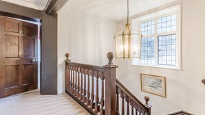 Una escalera con barandilla y balaustrada de madera, un candelabro, un cuadro en la pared y un ventanal de varios paneles.