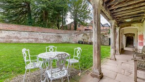 Un patio techado con una mesa y sillas, un muro de ladrillo y una zona con césped.