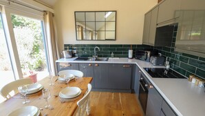 A modern kitchen with grey cabinets, a wooden dining table set for four, and a large window with curtains.