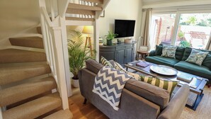 A living room with a staircase, a sofa, a coffee table, and a television.