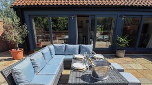 An outdoor patio with a wicker sofa, a dining table set with plates and glasses, and a champagne bucket.