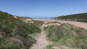 Un sentier qui longe la plage et mène à une étendue de sable fin, bordée de dunes, sous un ciel bleu et dégagé.