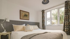 Une chambre à coucher avec un lit, une table de chevet avec une lampe, un tableau encadré au mur et une fenêtre avec des rideaux.