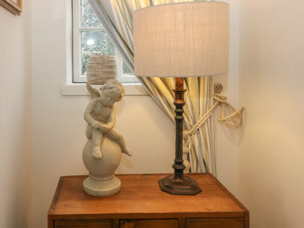 Une table de chevet en bois surmontée d’une sculpture en céramique blanche représentant une figure assise et d’une lampe de table avec un abat-jour en tissu.