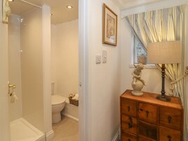 Un baño con ducha, inodoro y un armario de madera con cajones.