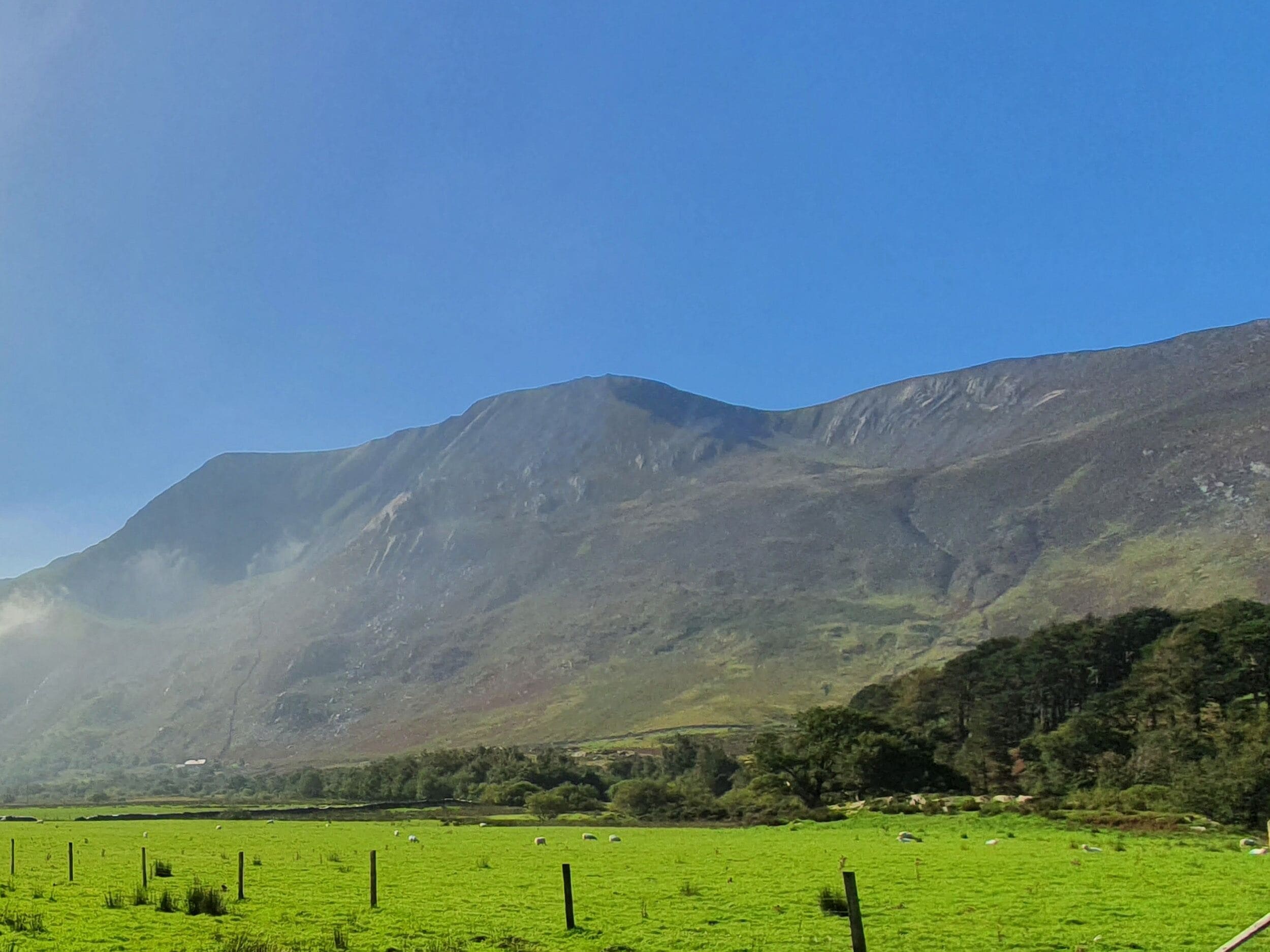 Un paisaje montañoso con un campo verde y una cerca.
